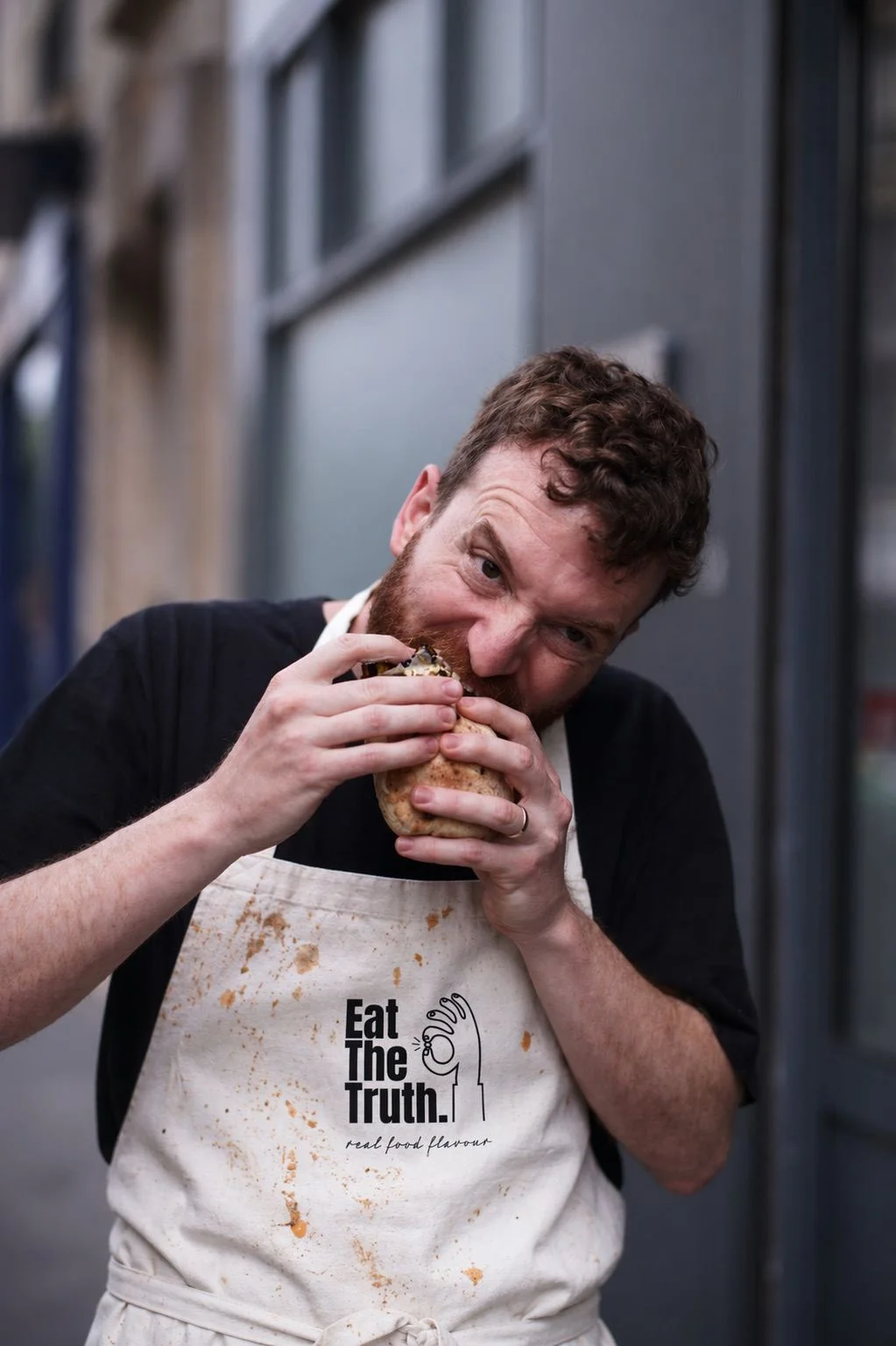 Chef en tablier Eat The Truth mordant dans un plat, illustrant la passion pour la vraie saveur