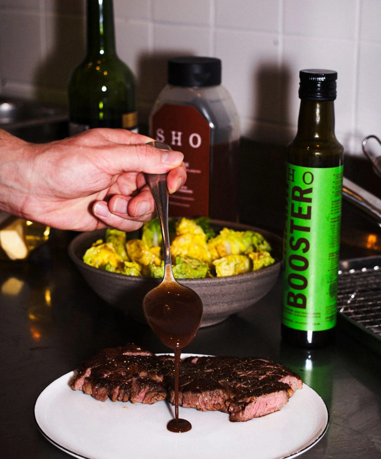 SHO Umami Booster sauce drizzled over a grilled steak with the product bottle in the background