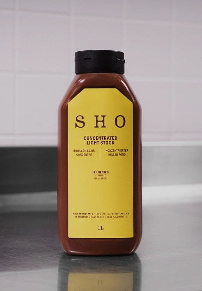 Bouteille de fond clair concentré SHO présentée comme base culinaire sur un plan de travail
